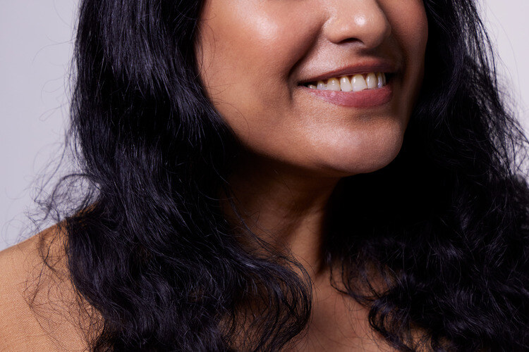 Photo of a dark skinned, dark haired woman smiling and wearing a brown dress